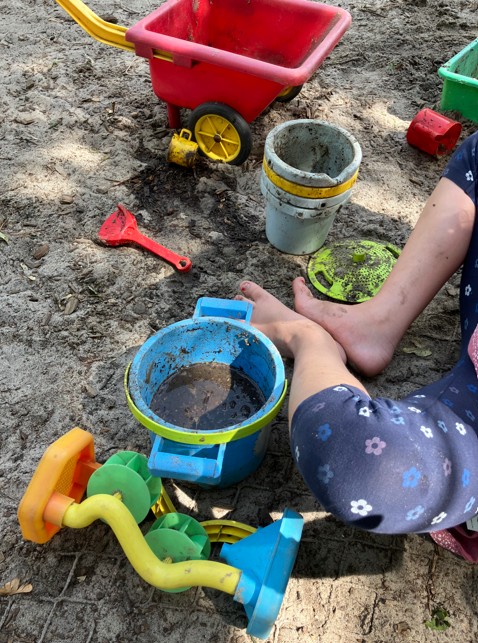 Kind spielt mit Sandspielsachen im Sand.